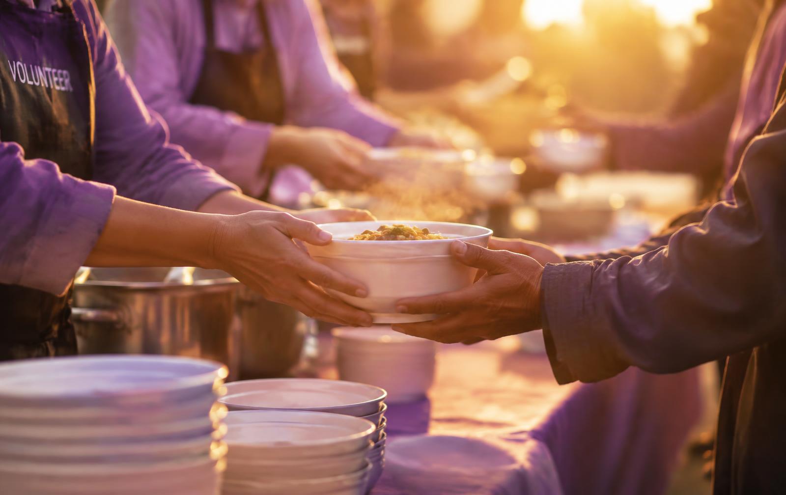 Volunteers handing a warm bowl of food across a community table